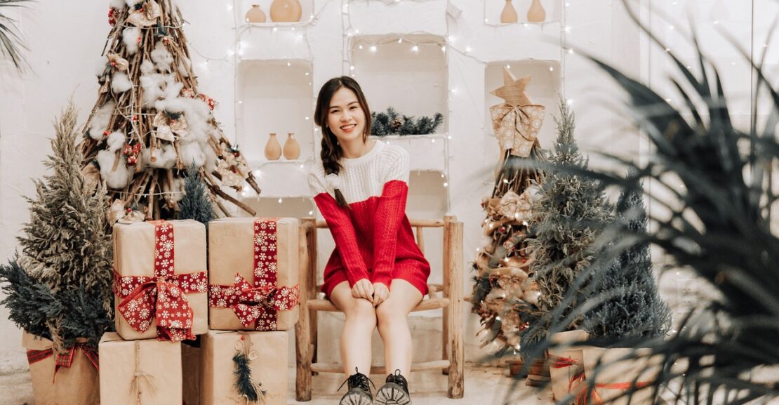 a young lady sitting beside a christmas tree and presents
