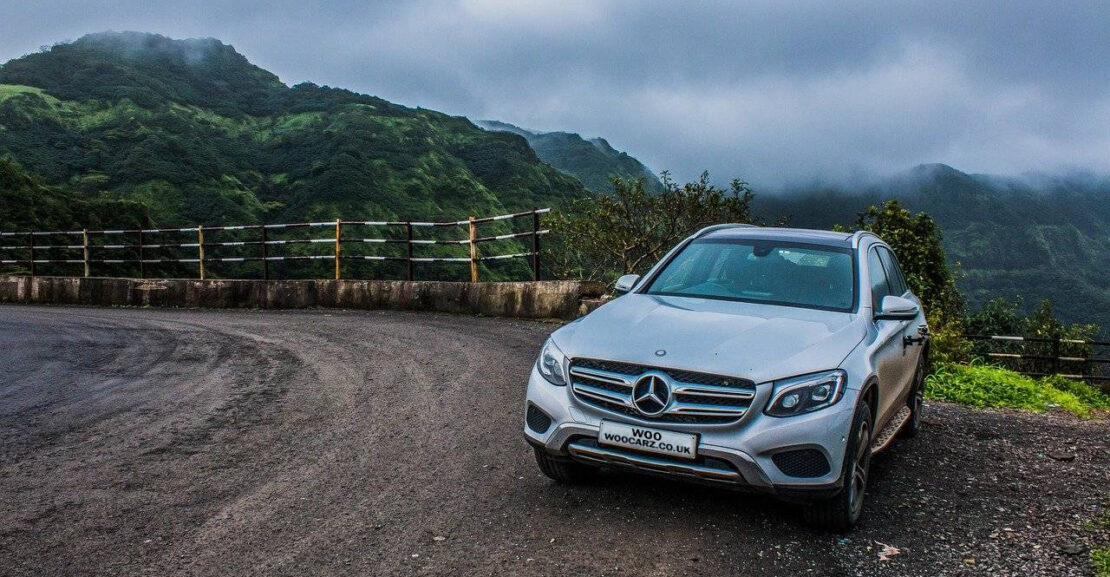 image of a mercedes parked with clouds and hills in the background